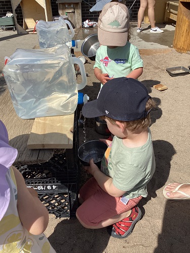 Children in the sandbox getting water out of a large jug