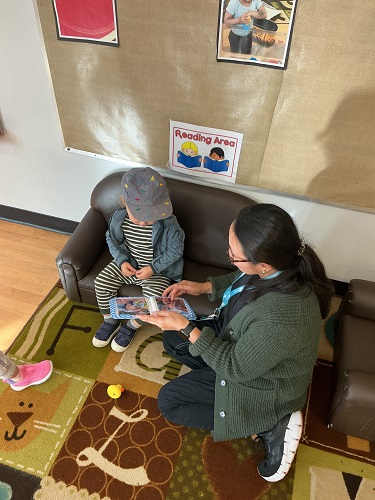 one Toddler and educator sitting on the couch looking at a photo book together