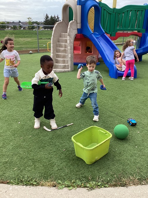 children playing a game with bean bags and a bucket outside