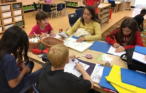 children sitting around a table and writing their journal entries