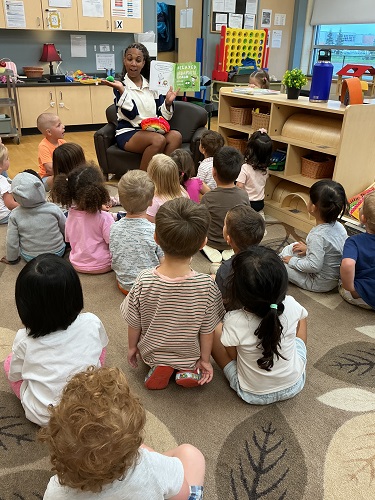 A group of children sitting on the carpet looking at an educator who is reading a story