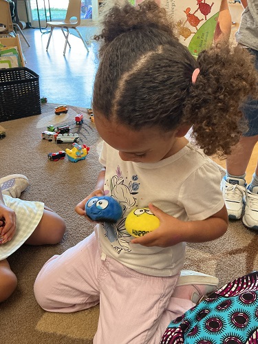 A child looking down at two toys in their hand, one is yellow one is blue