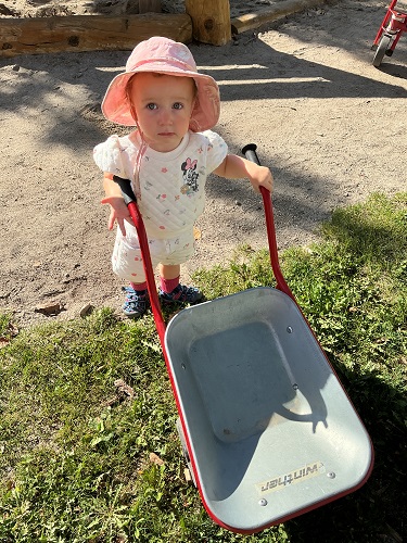 A child holding onto the handles of a wheelbarrow