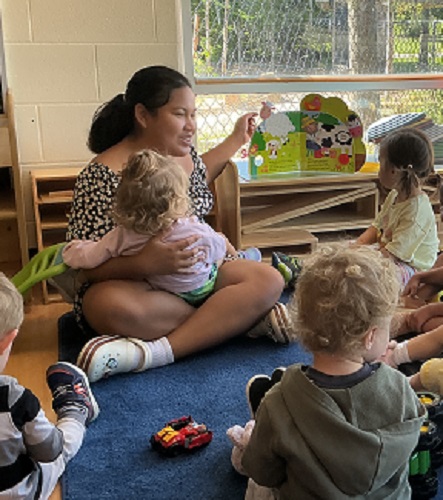 An educator sitting on the carpet reading a story to a small group of children