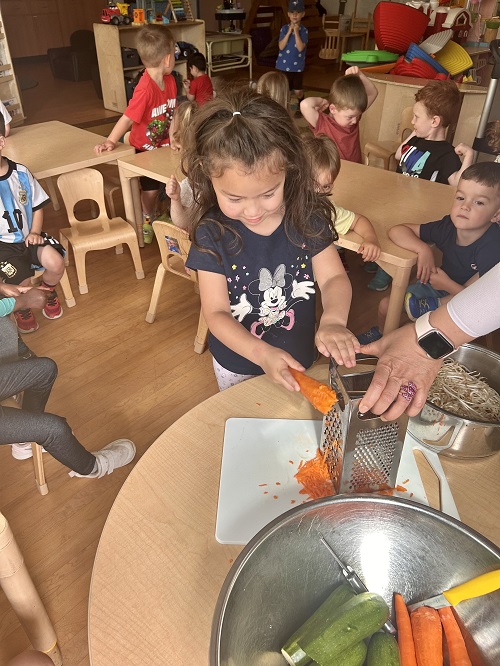 A child cutting vegetables with the help of an educator