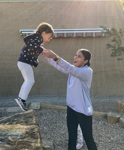 Educator assisting preschool child jumping off a log